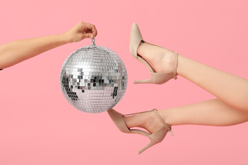 Female legs in trendy high heels and hand with disco ball on pink background