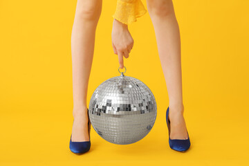 Female legs in trendy high heels with disco ball on yellow background