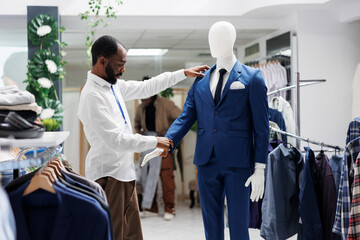 Boutique assistant checking mannequin dressed in formal menswear latest collection. African...