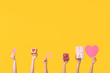Female hands with paper hearts and gift boxes on yellow background. Valentine's Day celebration