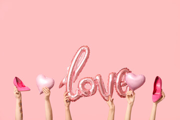 Female hands with high heels, balloons in shape of word LOVE and hearts on pink background. Valentine's Day celebration