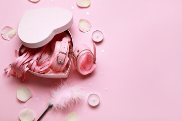 Heart shaped gift box with with sex toys, candles and rose petals on pink background