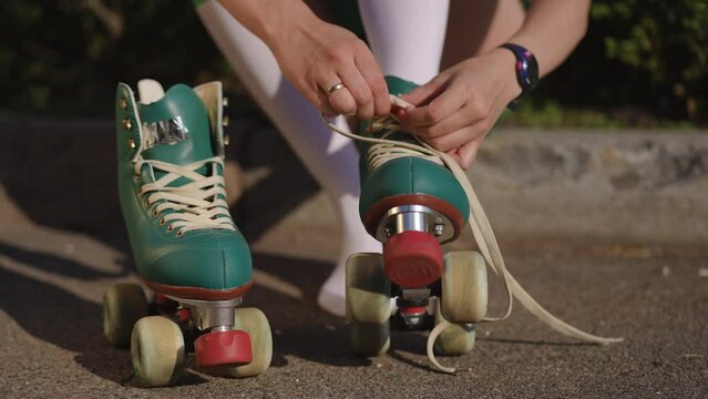 A woman sitting outdoors on a bright sunny day puts a roller skate on her foot and lace it up. Close-up