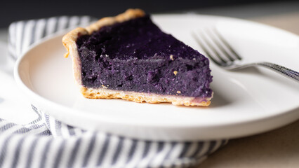 Purple yam pie on a white ceramic plate with fork.