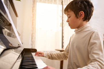 Teen boy pianist playing grand piano during music lesson at home. A teenager is practicing on chord...