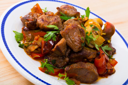 Cooked fried pork meat with peppers, mushrooms and greens on plate