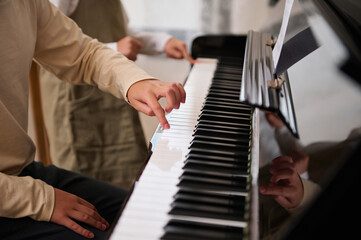 Children hands touching white and black piano keys while performing a musical composition, playing...