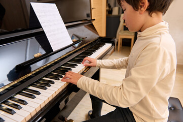 Handsome teenage schoolboy learning music at home, playing grand piano