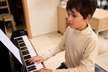 Handsome school child boy touching black and white keys, preforming classical melody during music...