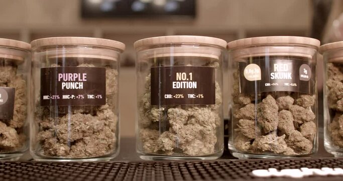 Glass jars with different varieties of CBD cannabis. Selecting a product for the consumer at a store window. Attracting the buyer's attention.