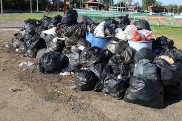 Piles of garbage on the ground. Closeup of black garbage bags and overflowing trash piled up on a...