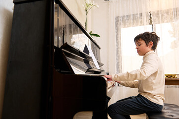 Adorable boy pianist, musician expressing positive emotions while enjoys playing grand piano at...