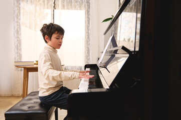 Confident authentic portrait of a handsome serene teenage boy playing piano at home. Culture and...