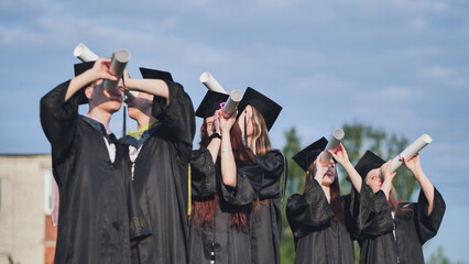 Cheerful graduates on a sunny day look through diplomas like a telescope.