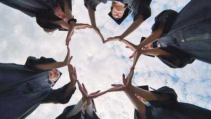 Students graduating from the college make a heart out of their hands.