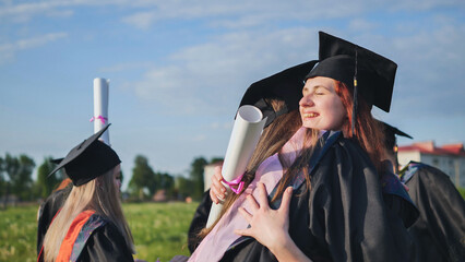 Two college graduates girls hugging on a sunny day.