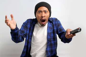 An enraged Asian man, dressed in a beanie hat and casual shirt, shouts in anger while watching a...