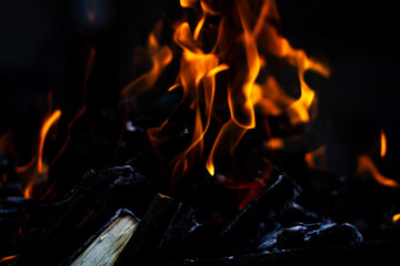 Horizontal color photo of an open fire, coals, ashes, firewood close up with a darkened black background. Selective focus on the main object.