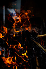 Vertical color photo of an open fire, coals, ashes, wood and smoke close up against a darkened black background. Selective focus on the main object.
