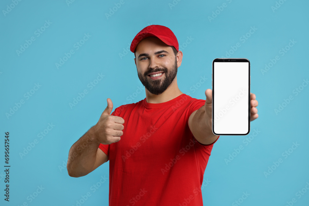 Sticker Happy courier holding smartphone with empty screen and showing thumbs up on light blue background