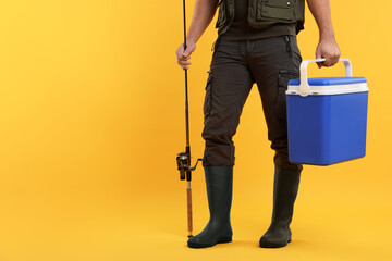 Fisherman with fishing rod and cool box on yellow background, closeup. Space. for text