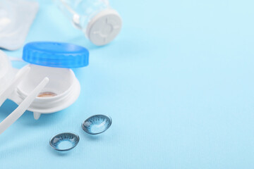 Case with color contact lenses and tweezers on light blue background, closeup. Space for text