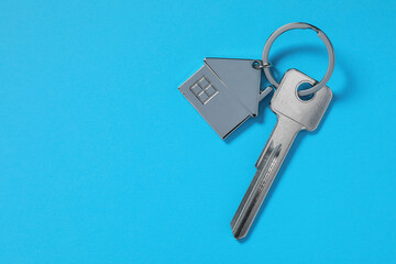 Metallic key with keychain in shape of house on light blue background, top view. Space for text
