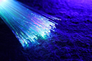 Optical fiber strands transmitting different color lights on textured background, closeup. Space...