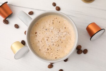 Cup of coffee, capsules and beans on white wooden table, flat lay