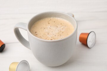 Cup of coffee and capsules on white table, closeup