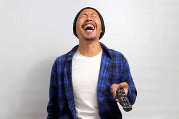 Happy young Asian man, dressed in a beanie hat and casual shirt, bursts into laughter while...