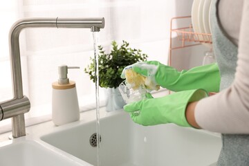 Woman washing glass at sink in kitchen, closeup