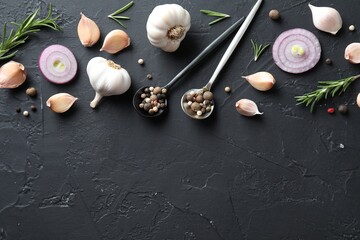 Fresh raw garlic, onion rings and spices on black table, flat lay. Space for text