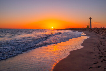 View on the lighthouse, the ocean waves and the beach at sunset with beautiful colours in Morro Jable, Jandia on the Canary Island Fuerteventura, Spain.
