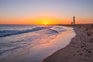 View on the lighthouse, the ocean waves and the beach at sunset with beautiful colours in Morro Jable, Jandia on the Canary Island Fuerteventura, Spain.