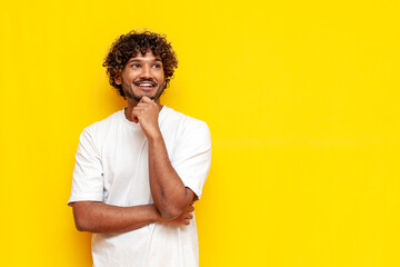 young indian pensive guy planning and dreaming over yellow isolated background and smiling
