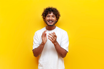 young indian guy laughing and cheering looking at the camera on a yellow isolated background