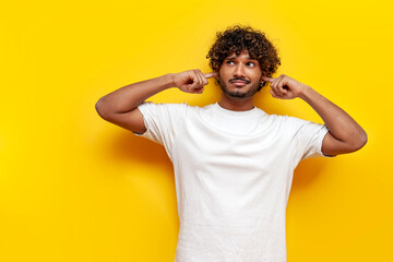 young indian guy avoids and ignores noise over yellow isolated background - obrazy, fototapety, plakaty