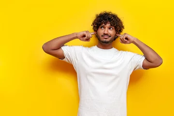 Fotobehang young indian guy avoids and ignores noise over yellow isolated background © Богдан Маліцький