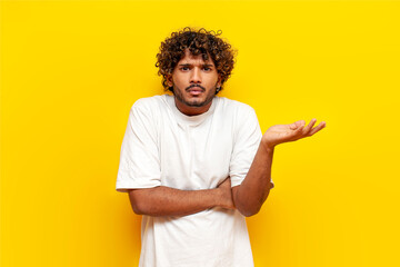 young indian uncertain guy doesn't know and shrugs over yellow isolated background, puzzled south asian man