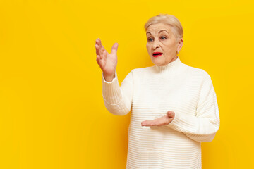 old grandmother in a white sweater screams and announces on a yellow isolated background