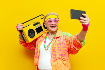 crazy old grandmother with tape recorder and smartphone in hipster clothes listens music on yellow...