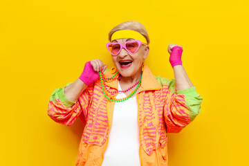 funny crazy old granny in sports hipster clothes rejoices at success and victory on a yellow isolated background - obrazy, fototapety, plakaty