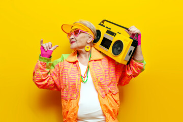 funny old granny with tape recorder in sports hipster clothes takes selfie online on yellow...