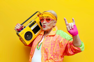 funny crazy old granny with tape recorder in sports hipster clothes listens to rock music on yellow background - obrazy, fototapety, plakaty