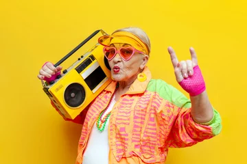Fotobehang funny crazy old granny with tape recorder in sports hipster clothes listens to rock music on yellow background © Богдан Маліцький