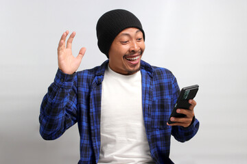 An astonished Asian man, dressed in a beanie hat and casual shirt, reacts with surprise to an...