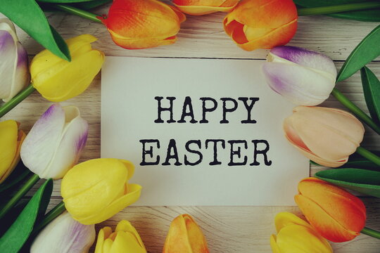 Happy Easter text message on paper card with tulip flowers top view on wooden background