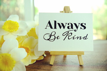 Always be kind text message on paper card with wooden easel on wooden table background, inspiration...