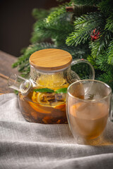 Orange fragrant tea in a glass teapot on the background of a Christmas tree. Cozy warm festive atmosphere